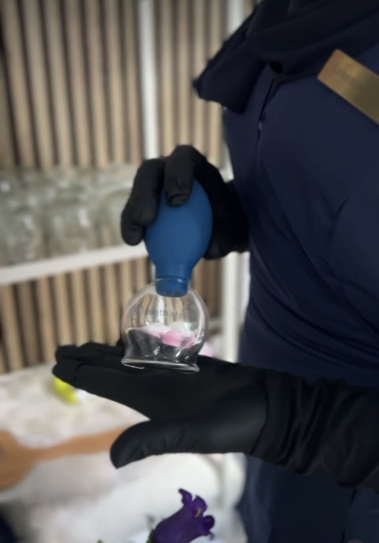 Handen in zwarte handschoenen zetten een glazen cup met een blauwe pompbal klaar